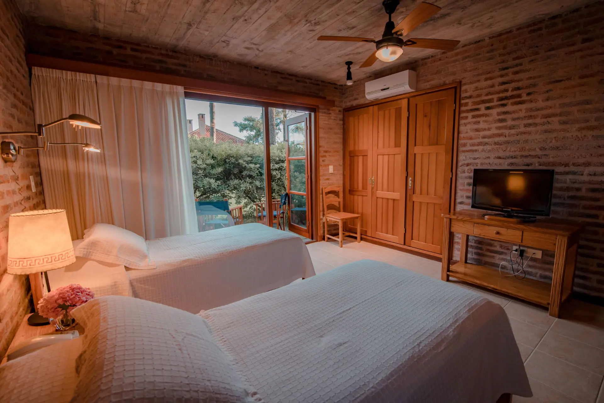 Habitación de la cabaña con dos camas, paredes de ladrillo y salida al jardín
